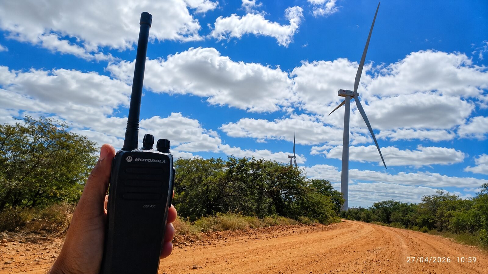 Rádio Motorola em uso em campo com parque eólico ao fundo